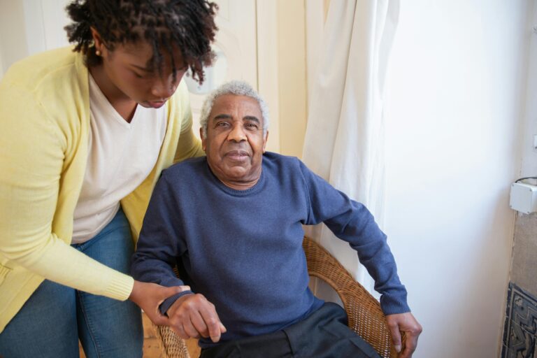 A woman helping an older man sit in a chair.